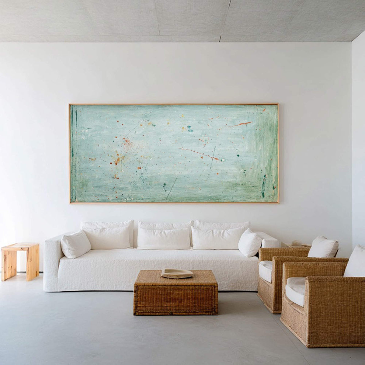 May include: A modern living room featuring a large abstract painting in shades of blue and green with a wooden frame. A white sofa with throw pillows, two wicker armchairs, a wicker coffee table, and a small wooden side table complete the decor.