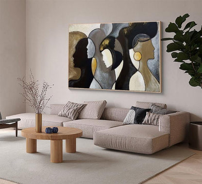 May include: Abstract art piece featuring three stylized female profiles in shades of black, gold, and gray. The artwork is framed and hangs above a beige sectional sofa in a modern living room setting.