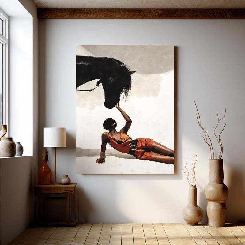 May include: A large canvas print depicts a person in an orange outfit interacting with a black horse. The person is lying down, reaching up to touch the horse's head. The background is a neutral color, and the artwork is displayed in a room with wooden floors.