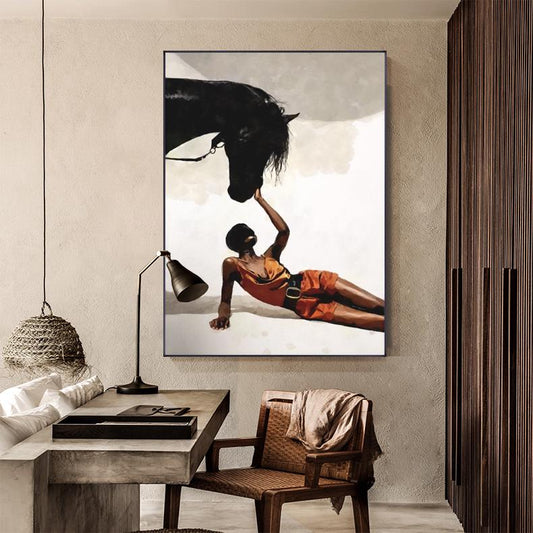 May include: An artistic painting depicts a person in orange attire interacting with a black horse. The person is lying down, reaching up towards the horse's head. The artwork is framed and mounted on a wall, showcasing a modern aesthetic.