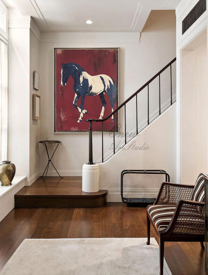 May include: Large framed painting of a horse in motion. The horse is depicted in white and navy blue against a deep red background. The artwork hangs on a white wall in a well-lit hallway with a staircase and a striped chair.