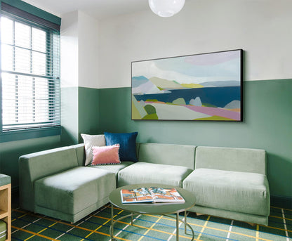 May include: A modern living room with a sage green sectional sofa, pillows, and a round coffee table. A colorful abstract landscape painting hangs above the sofa. The room has a green and yellow patterned rug and a window with blinds.