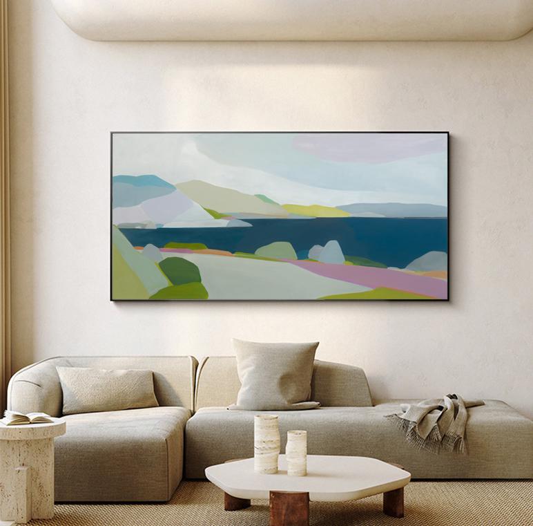 May include: Abstract landscape painting with a black frame. The artwork features a serene coastal scene with mountains, water, and colorful fields. The color palette includes blues, greens, pinks, and yellows, creating a calming aesthetic.