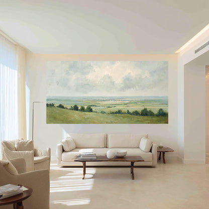 May include: A large landscape painting depicting a serene vista of rolling green hills, trees, and a distant body of water under a cloudy sky. The artwork is mounted on a white wall in a modern living room setting.