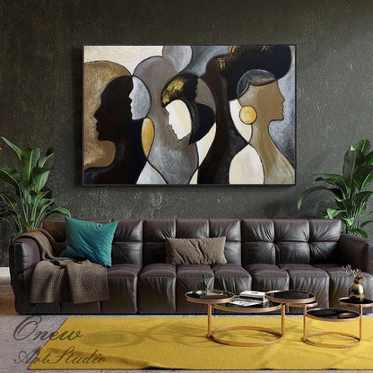 May include: Abstract painting featuring three stylized female profiles in shades of black, gold, and white. The artwork is framed in black and hangs above a brown leather sofa. The painting's style is modern and minimalist.