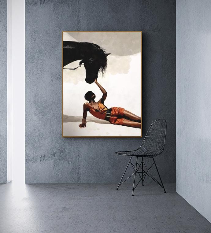 May include: An artistic print featuring a black horse and a person in orange attire. The person is lying down, reaching towards the horse's head. The artwork is framed in a gold border, set against a neutral background.