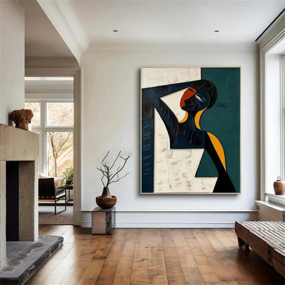 May include: Abstract painting of a figure with a dark blue body, orange face, and yellow accents. The artwork is set against a white and teal background, framed in a dark blue border. The painting is displayed in a well-lit room with hardwood floors.
