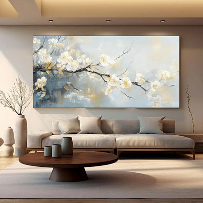 May include: A large rectangular canvas painting depicts a branch of white blossoms against a soft, abstract background of blues, grays, and yellows. The artwork hangs above a modern sofa with neutral-colored cushions, complemented by a round wooden coffee table.