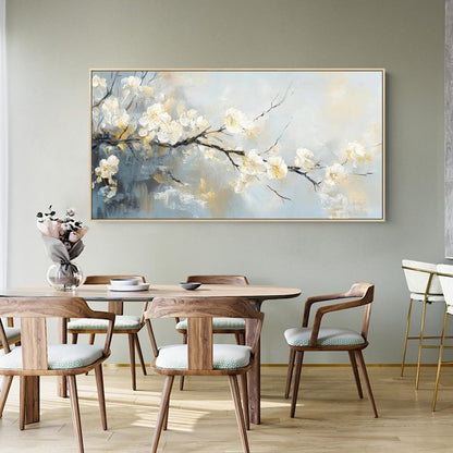 May include: A framed floral painting featuring white blossoms on a dark branch against a soft blue and gold background. The artwork hangs above a wooden dining table with matching chairs, creating a serene and elegant atmosphere.