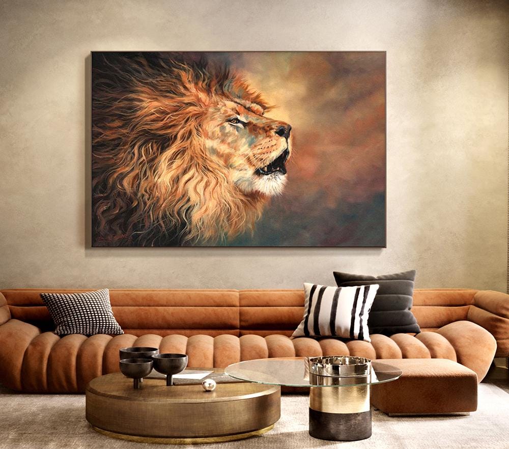 May include: A large, rectangular canvas print of a lion's head in profile. The lion has a full, flowing mane of orange and brown fur. The background is a blend of brown, orange, and blue hues, creating a dramatic effect. The artwork is displayed above a brown sofa.