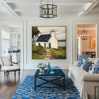 May include: A large square oil painting depicting a white cottage with a dark roof and a path, displayed on a white wall above a dark blue wooden coffee table. The artwork features muted tones of green, brown, and white in a landscape setting.