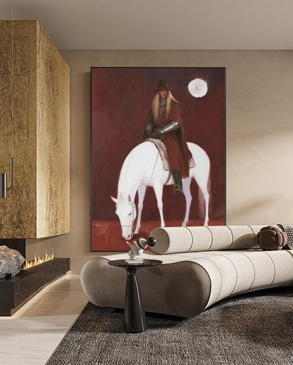 May include: A large framed painting depicts a person on a white horse against a deep red background. The person wears a brown hat and cloak. A white moon shape is in the upper right corner. The painting hangs above a modern sofa.