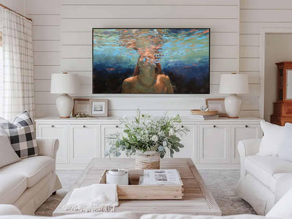 May include: Living room with white sofas, a wooden coffee table, and a large painting above a white cabinet. The painting depicts a person underwater. Two white lamps sit on the cabinet, and a vase of flowers is on the coffee table.