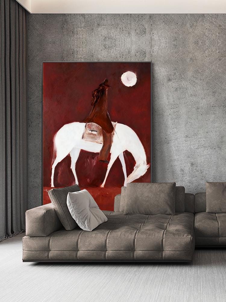 May include: An abstract painting depicts a rider on a white horse under a full moon against a deep red background. The rider is wearing a brown cloak. The artwork is displayed above a modern, gray sectional sofa.