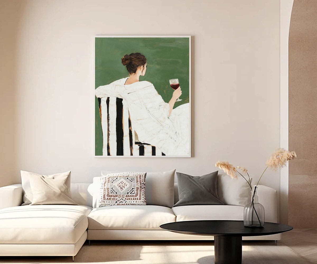 May include: A framed art print depicts a person seated in a chair, holding a glass of red wine. The chair has black and white striped upholstery. The background is a solid green color. The person is wearing white clothing.