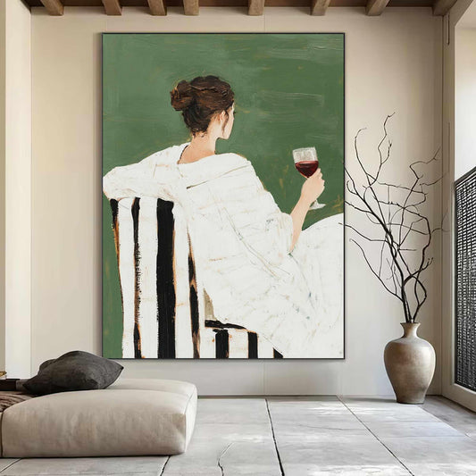 May include: An abstract painting depicts a person in a white dress seated in a chair with black and white stripes, holding a glass of red wine. The background is a solid green color. The artwork is displayed in a well-lit room with a neutral color palette.