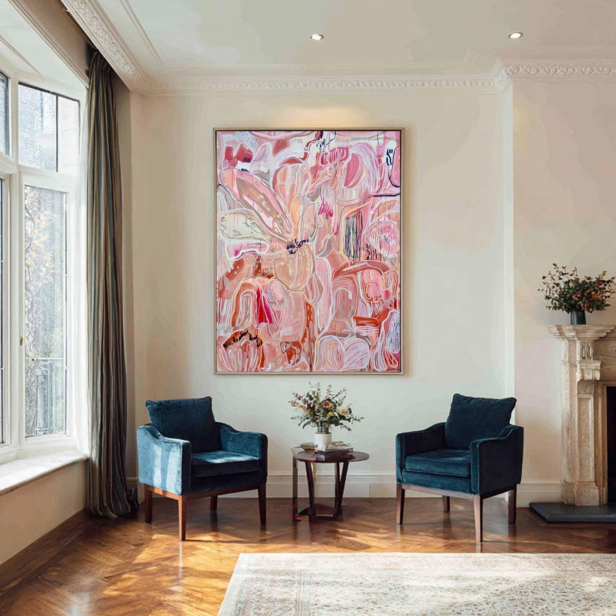 May include: An abstract painting with a floral theme dominates a living room. The artwork features shades of pink, peach, and white, framed in a gold tone. Two navy blue velvet armchairs face each other, with a small round table between them. The room has hardwood floors and a large window.