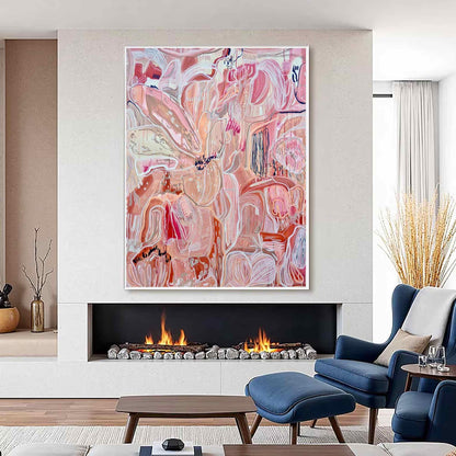 May include: Large abstract painting in a white frame. The artwork features a floral design with shades of pink, peach, and white. The painting hangs above a fireplace with a lit fire, complemented by blue armchairs and a footstool.