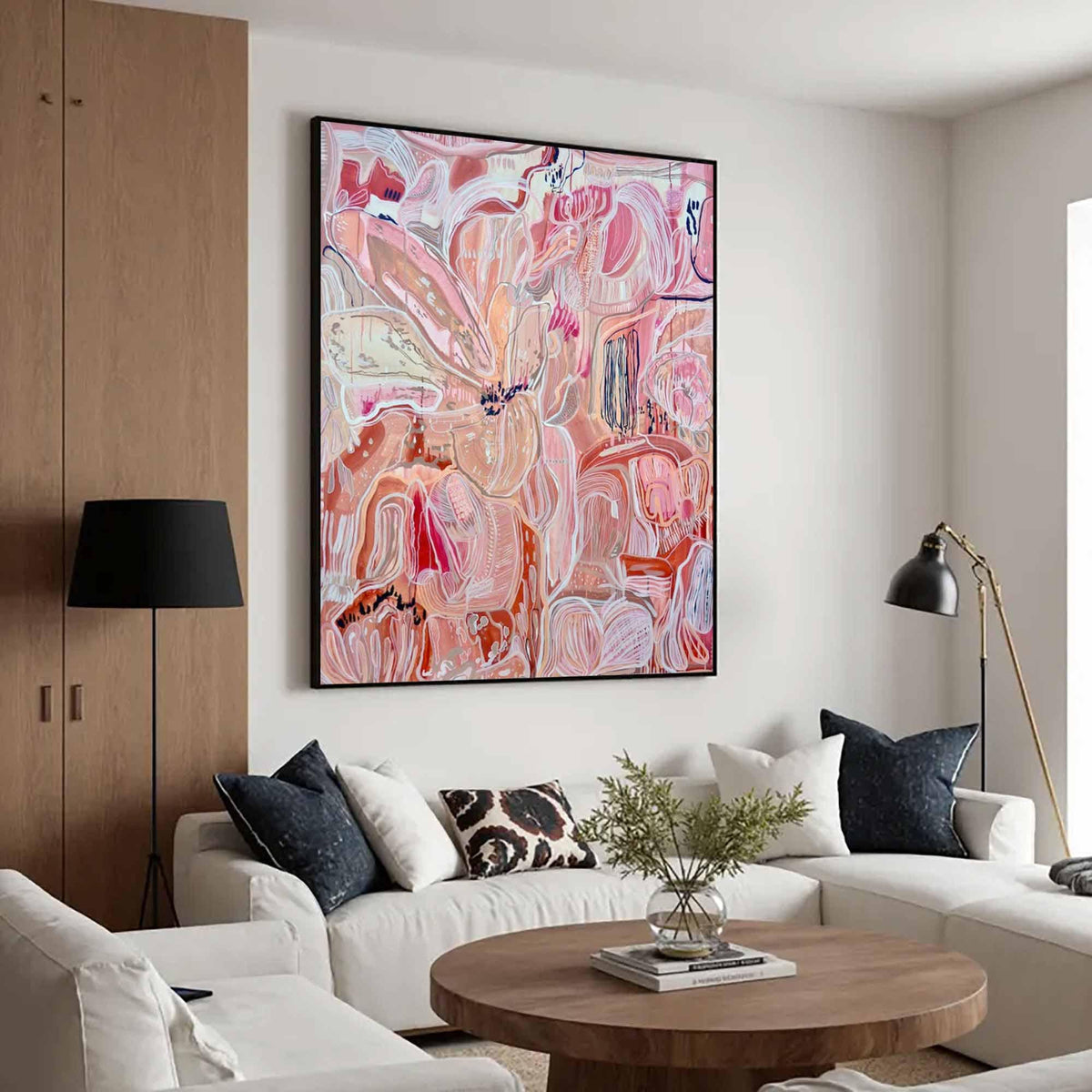 May include: Abstract floral painting in shades of pink, red, and white, framed in black. The artwork hangs above a white sofa with decorative pillows. A black floor lamp and a wooden coffee table complete the living room setting.