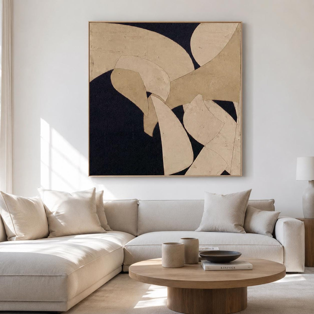 May include: Abstract art piece with a dark navy background and beige and off-white organic shapes. The artwork is framed in a light wood tone and hangs above a beige sectional sofa. The room is well-lit with natural light.