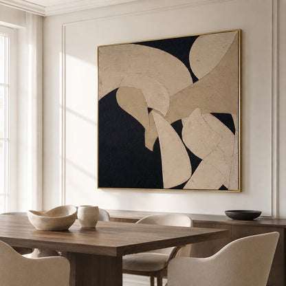 May include: Abstract art piece with a gold frame. The artwork features a composition of beige and black shapes. The painting is displayed in a well-lit room with a wooden dining table and chairs.
