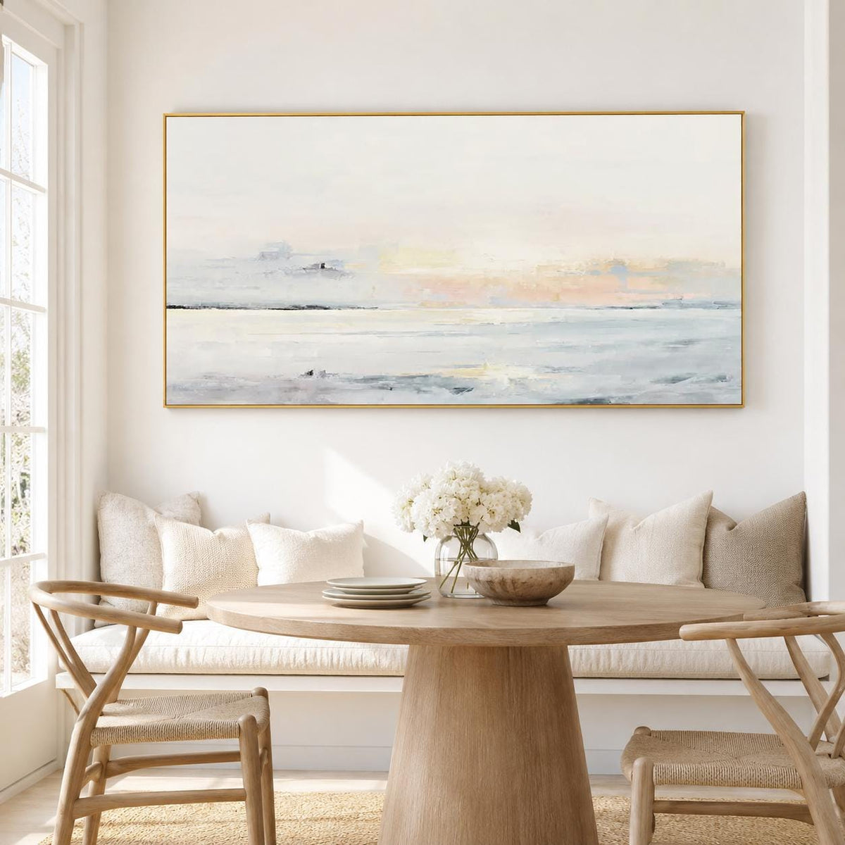 May include: A large rectangular landscape painting with a gold frame. The artwork depicts a serene coastal scene with soft pastel colors of white, blue, and peach. The painting hangs above a wooden dining table.