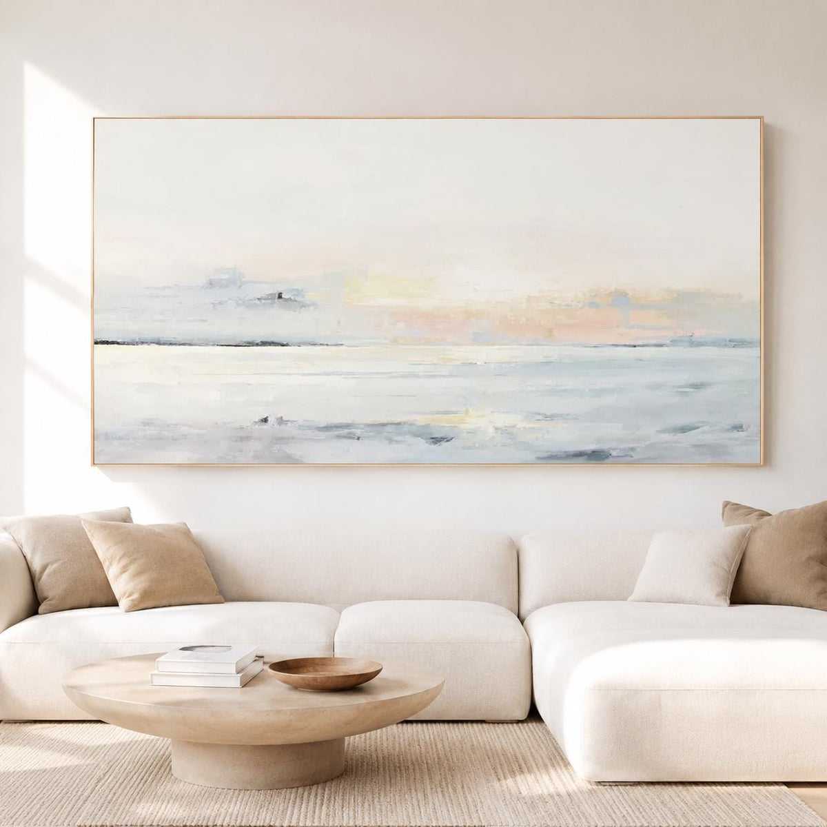 May include: Large abstract landscape painting in a gold frame. The artwork features a serene coastal scene with soft pastel colors, including shades of white, blue, and peach. The painting is displayed above a white sectional sofa.