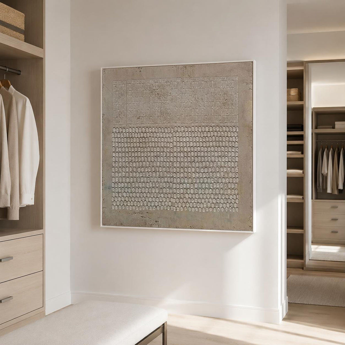 May include: A square wall art piece featuring a textured beige and gray surface with a top section of vertical lines and a bottom section of repeating oval shapes, all enclosed within a thin white frame, displayed on a plain wall.