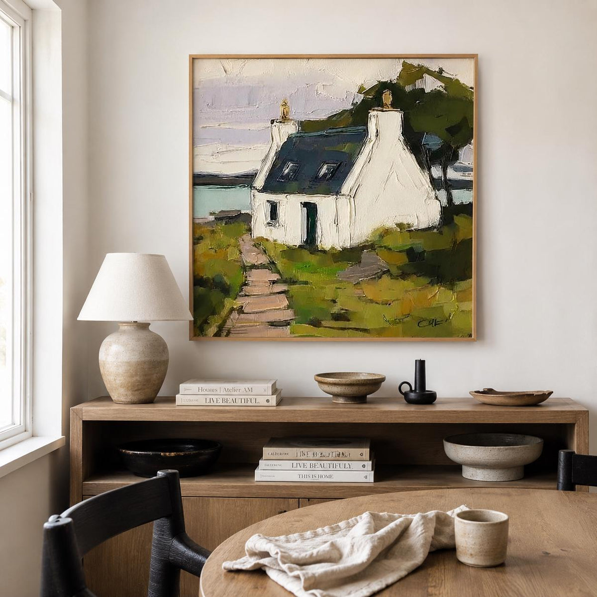 May include: A square oil painting featuring a white cottage with a dark blue roof situated on a grassy landscape with a stone path leading to the entrance. The scene includes a body of water in the background under a pale sky, rendered with thick, visible brushstrokes and a palette of greens, whites, and blues.