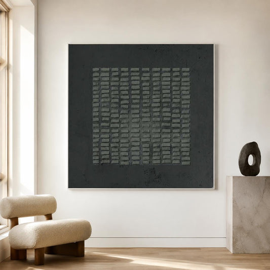 May include: A large square wall art piece featuring a dark charcoal background with a central grid of raised, rectangular gray blocks. The artwork is framed in a thin white border and displays a textured, matte finish across the entire surface.
