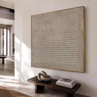 May include: A large square wall art piece featuring a textured beige and off-white surface with a geometric pattern of vertical lines on the top half and a grid of small raised circular shapes on the bottom half, framed in a thin gold metal frame.