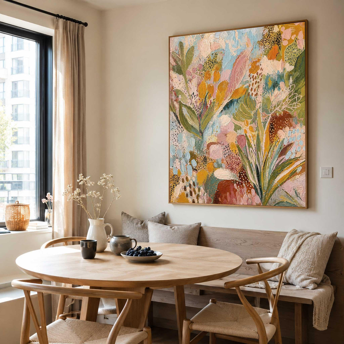 May include: A large rectangular canvas painting featuring an abstract botanical composition with layers of mustard yellow, sage green, soft pink, and sky blue paint, displayed in a thin wooden frame on a light-colored wall above a wooden dining bench.