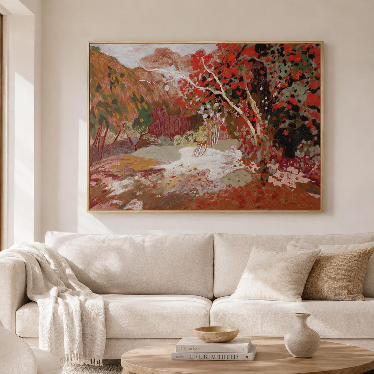 May include: A rectangular landscape painting in a thin gold frame featuring a vibrant autumn scene with deep red foliage, textured brushstrokes, and earthy tones of brown, green, and cream, displayed on a wall above a neutral-colored sofa.