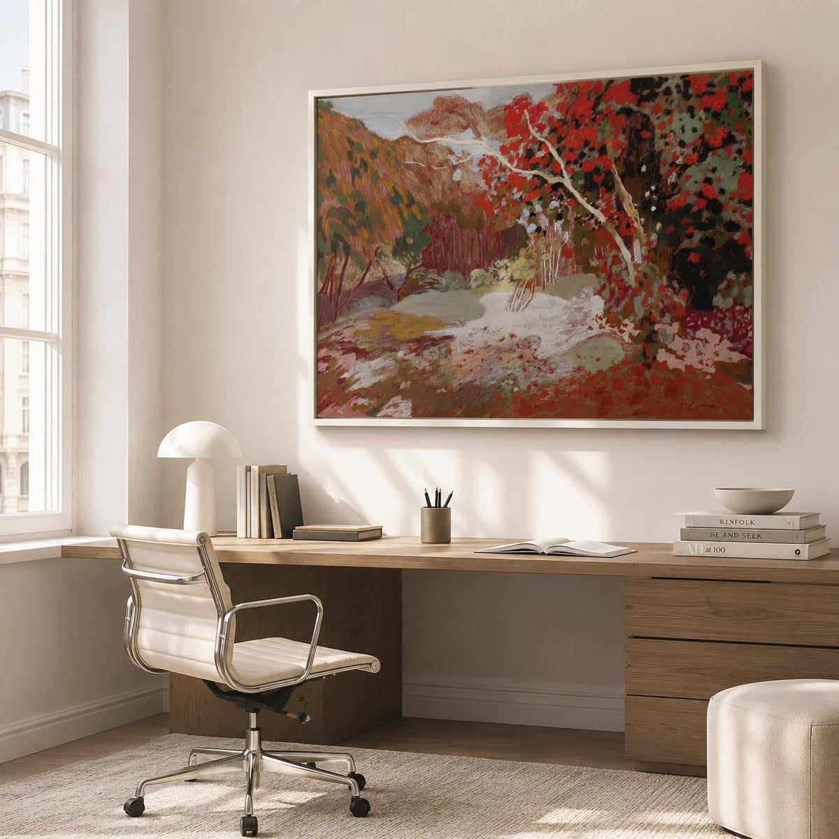May include: A rectangular wall art piece in a white frame featuring an impressionistic landscape painting with vibrant red foliage, muted green tones, and earthy brown mountains under a soft sky, displayed above a wooden desk in a bright room.