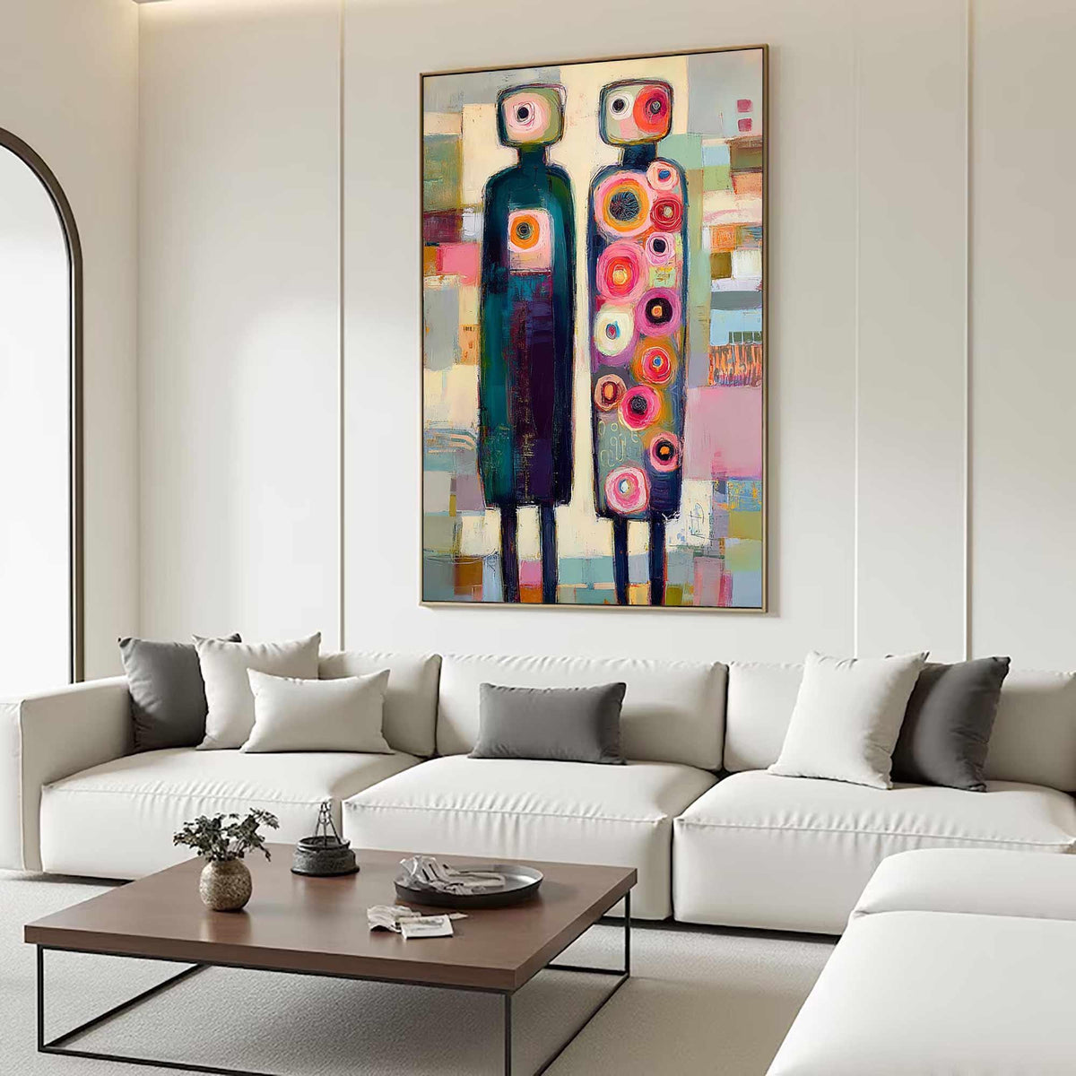 May include: Abstract art painting featuring two stylized figures with rectangular heads and elongated bodies. The figures are in front of a colorful background with geometric shapes. The painting is framed and hangs above a white sofa.