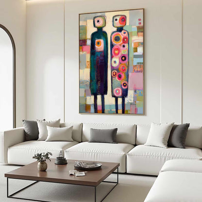 May include: Abstract art painting featuring two stylized figures with rectangular heads and elongated bodies. The figures are in front of a colorful background with geometric shapes. The painting is framed and hangs above a white sofa.