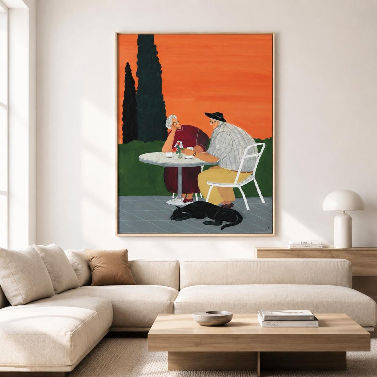 May include: A framed wall art print depicting two people sitting at a round white table outdoors against a vibrant orange sky. One person wears a dark red outfit, the other a plaid shirt and yellow trousers. A black dog lies on the ground nearby.