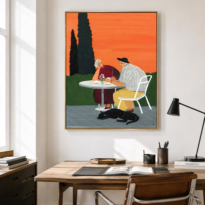 May include: A framed wall art print depicting two people sitting at a round table outdoors against a vibrant orange sky. One person wears a dark red top, the other a plaid shirt and yellow trousers. A black cat rests on the ground nearby.