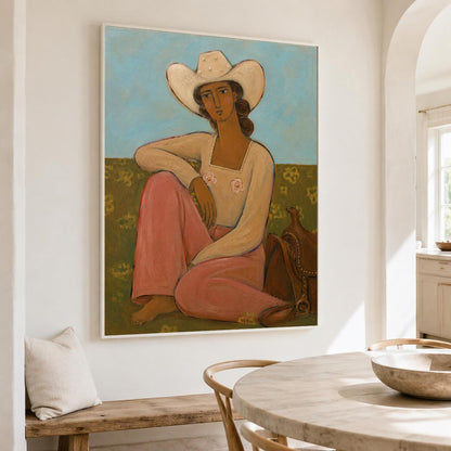 May include: A framed painting depicting a figure wearing a white cowboy hat, a long-sleeved cream top with two small pink flower details, and loose pink trousers. The figure sits on a dark olive green ground against a light blue sky background.