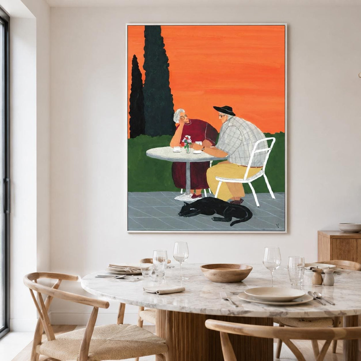 May include: A framed wall art print depicting two people sitting at a round white table on a patio. One person wears a maroon dress, the other a plaid shirt and yellow trousers. A black cat lies on the ground. The background features dark green trees and a vibrant orange sky.