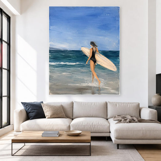 May include: A framed oil painting depicting a person in a black swimsuit walking into the ocean while carrying a light-colored surfboard. The scene features a bright blue sky, deep blue sea waves, and a sandy beach rendered in textured brushstrokes.