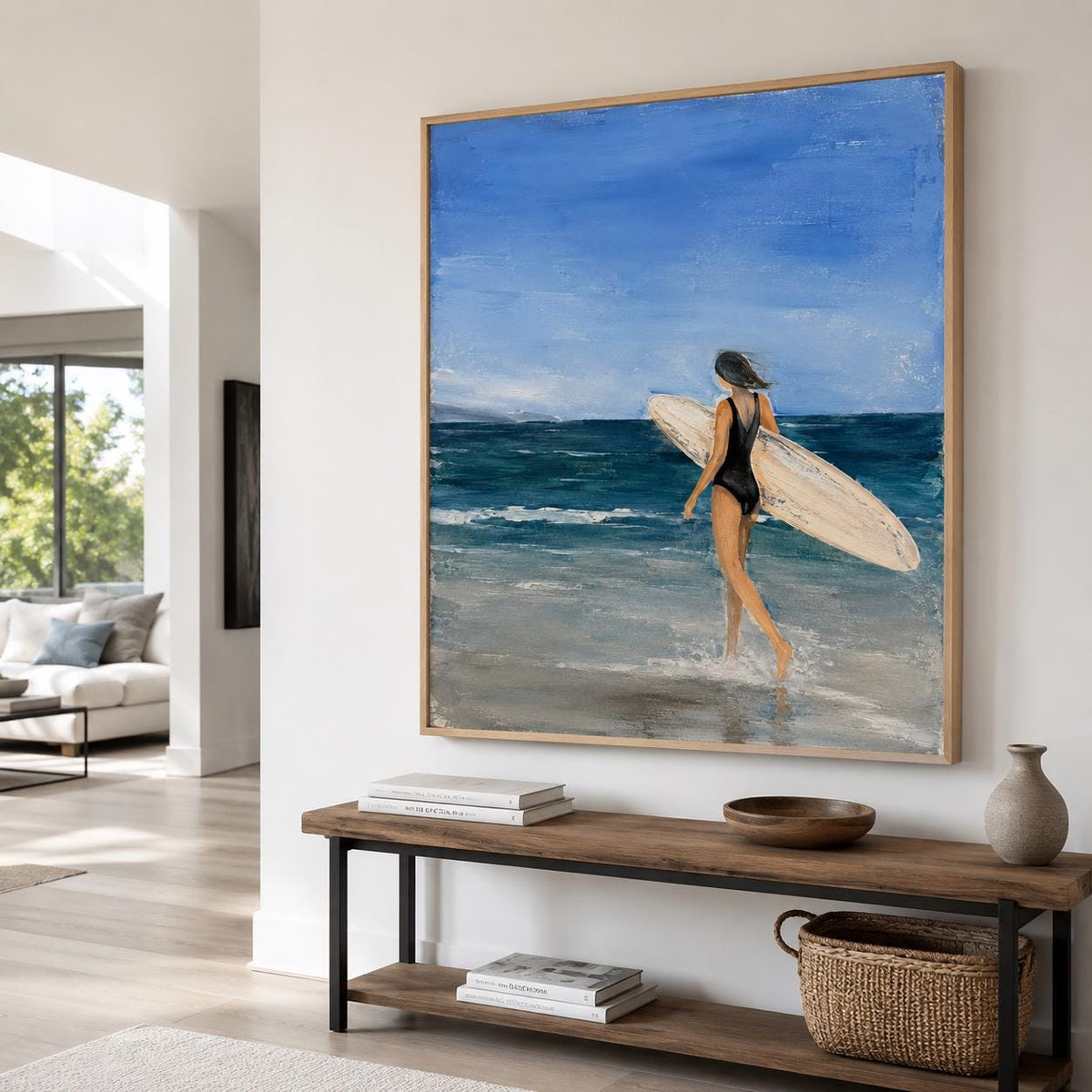 May include: A framed oil painting depicting a person in a black swimsuit walking into the ocean while carrying a surfboard. The scene features a bright blue sky, deep blue sea waves, and a sandy beach rendered with visible brushstrokes.