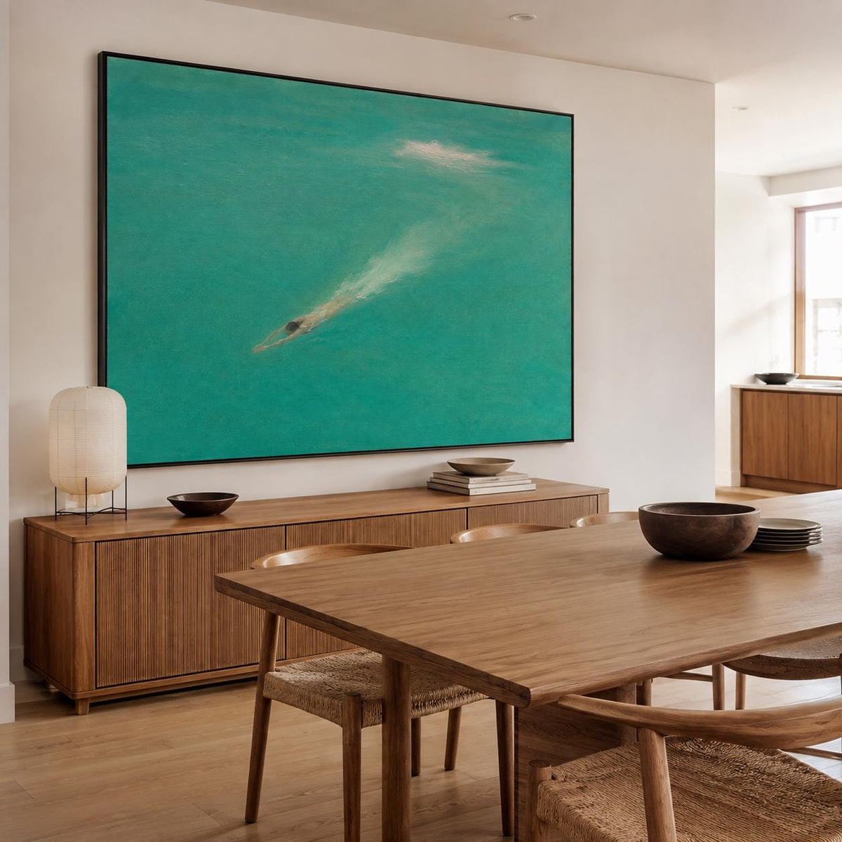May include: A large rectangular wall art piece featuring a vibrant turquoise sea with a single swimmer creating a white wake. The painting is framed in a thin black border and hangs above a long wooden sideboard in a bright, open room.