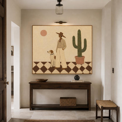 May include: A rectangular wall art print featuring a person in a wide-brimmed hat and striped shirt standing with a dog on a black and white checkered floor. A tall green cactus in a terracotta pot and a pale pink sun are visible in the background.