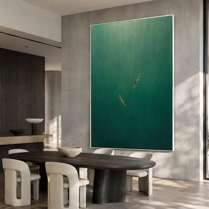 May include: A large rectangular wall art piece featuring a deep emerald green gradient background with two small figures swimming in the center. The artwork is displayed in a white frame and hangs on a textured gray wall above a dark wooden dining table.