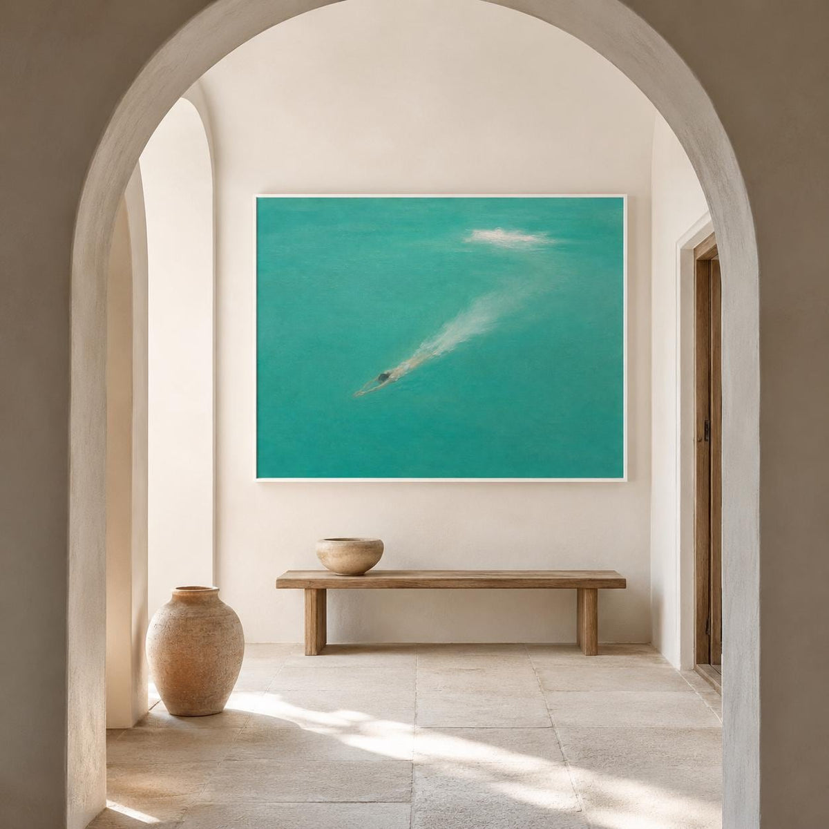 May include: A large rectangular wall art piece featuring a turquoise ocean scene with a swimmer creating a white wake, displayed above a long wooden bench and a rounded terracotta-colored floor vase in a neutral-toned arched hallway.