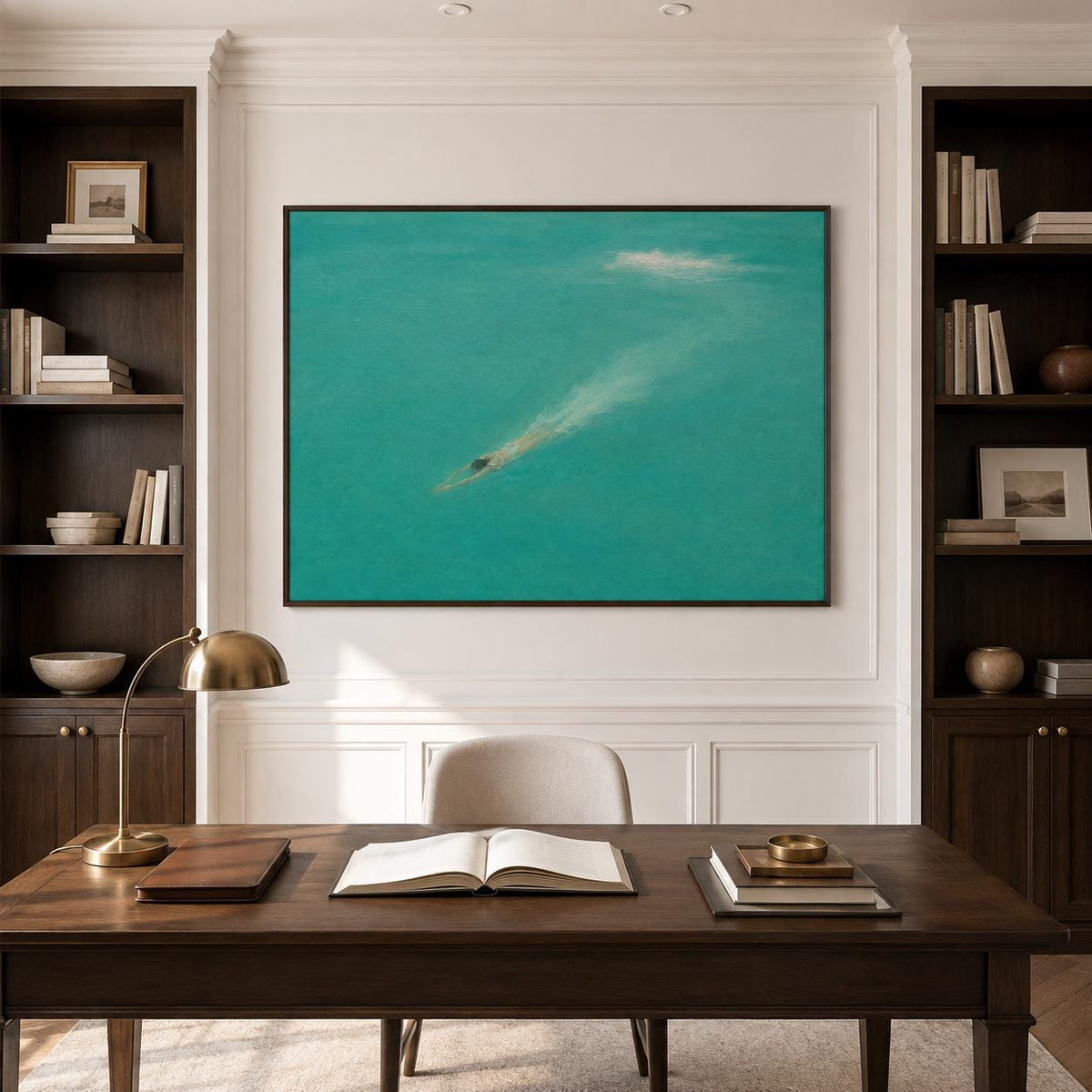 May include: A large rectangular wall art piece featuring a turquoise sea with a small dark swimmer creating a white wake, framed in dark wood. The artwork is centered above a wooden desk with an open book, a brass lamp, and stacked items.