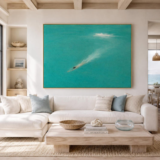 May include: A large rectangular wall art piece featuring a swimmer diving into vibrant turquoise water, creating a white splash trail. The painting is framed in a thin gold border and is displayed above a white sectional sofa with various pillows.