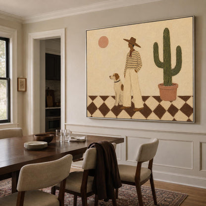 May include: A large rectangular wall art print featuring a person in a wide-brimmed hat and striped shirt standing next to a dog on a checkered floor. A tall green cactus in a terracotta pot and a pale pink sun are visible against a beige background.