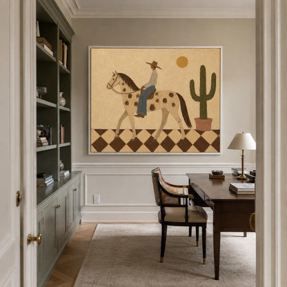 May include: A framed wall art print featuring a stylized illustration of a person in a hat riding a spotted horse across a brown and white checkered floor. A tall green cactus in a pot and a yellow sun are visible against a tan background.